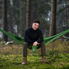 Mies istuu metsässä vihreällä ulkona riippumatolla Alpin Loackerilta, retkeilyriippumatto 